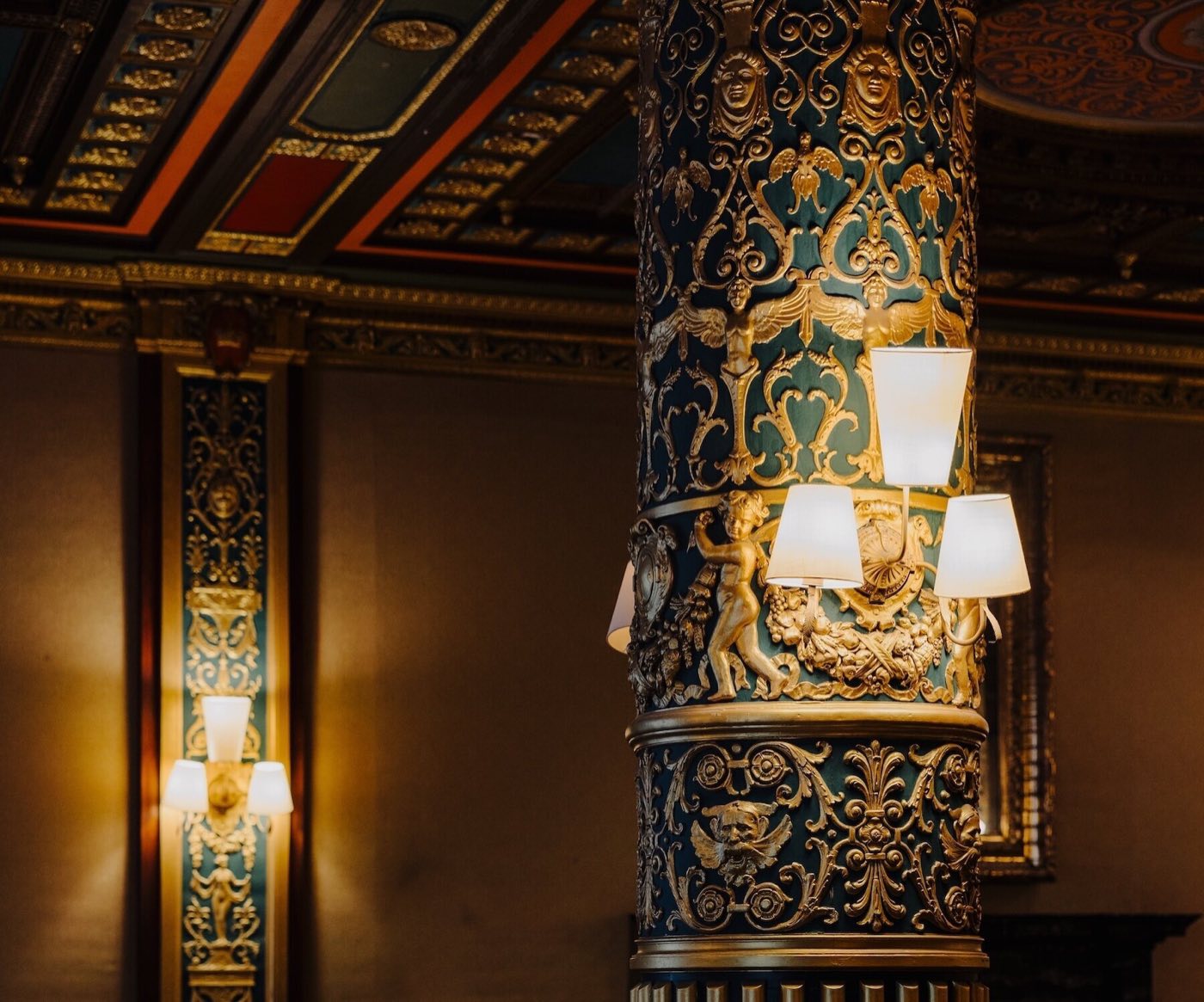 Close view of a carved and gilded ballroom column with lit sconces