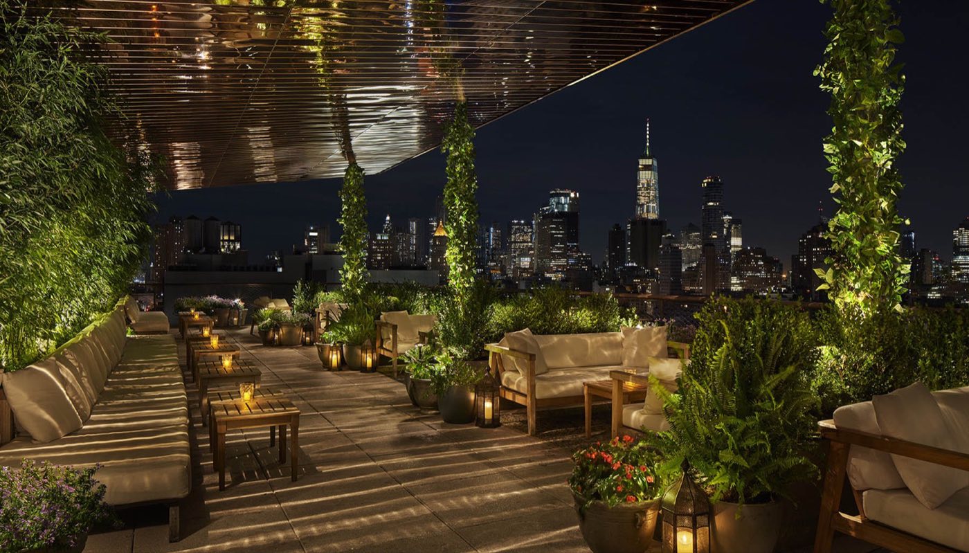 Rooftop terrace at night with planted walls, lounge seating and skyline views