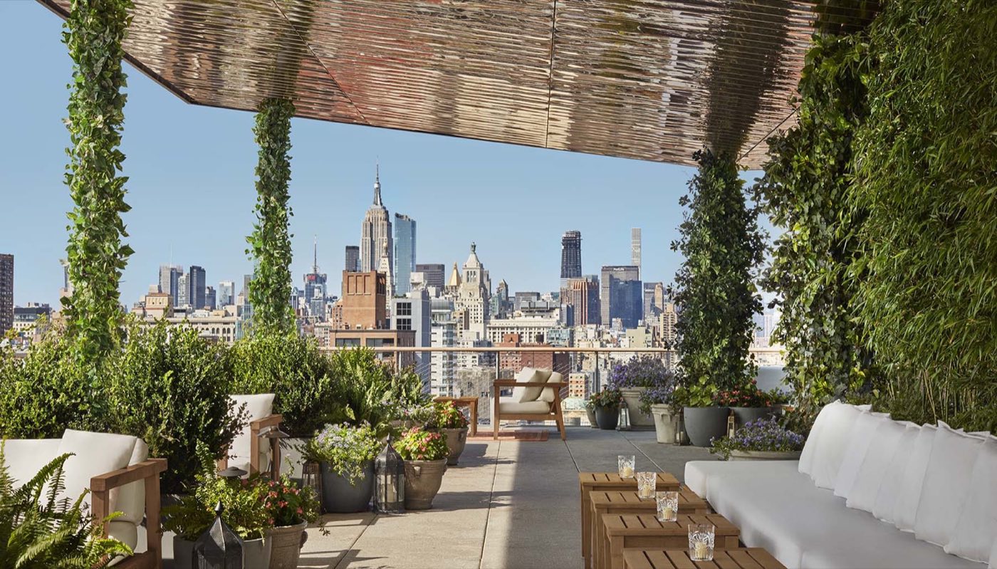 Covered rooftop terrace by day with white banquettes, greenery and Midtown views