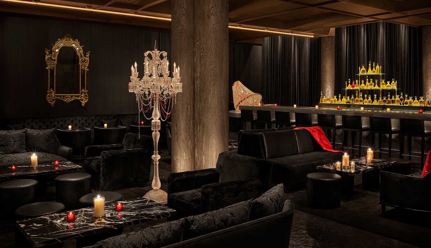 Dark lounge with velvet sofas, a candelabra and a long backlit bar