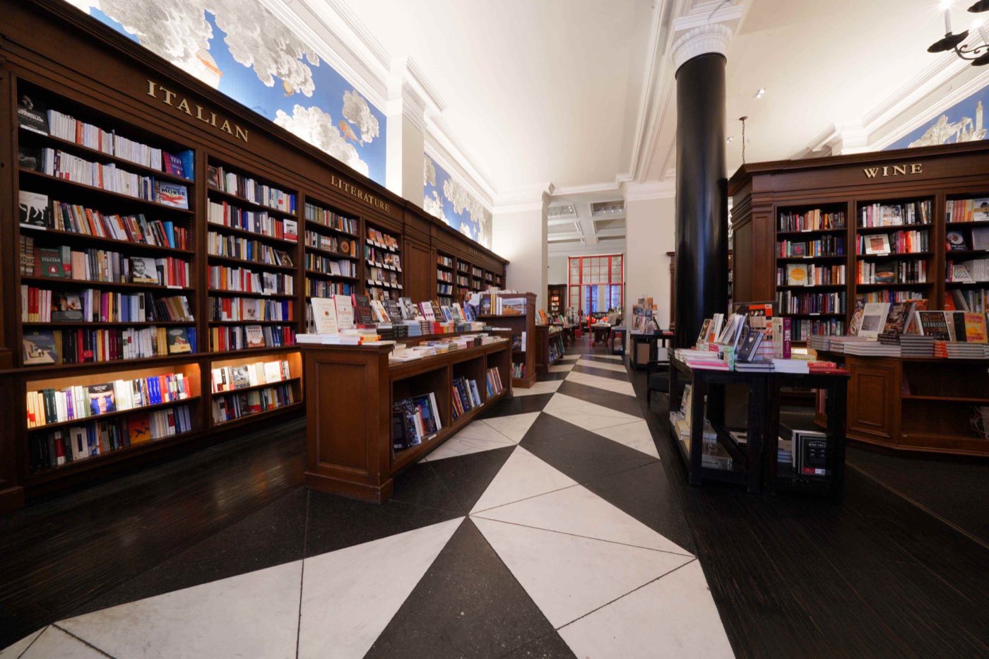 Long bookstore room with wood shelves, painted panels and a black and white patterned floor