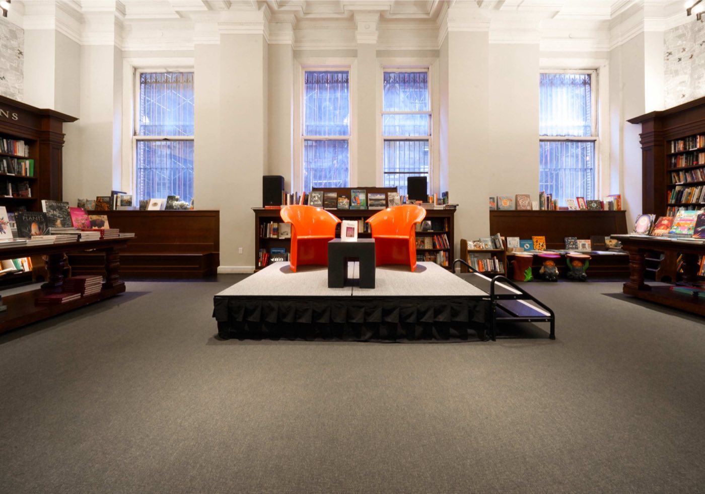 Salon with tall windows and a low stage set with two chairs for a talk