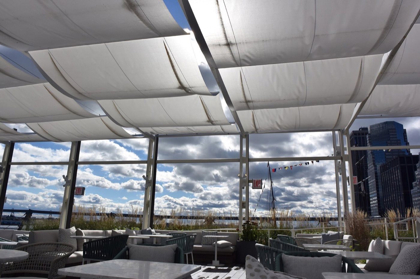 Covered rooftop lounge with sofas and harbor views through glass walls