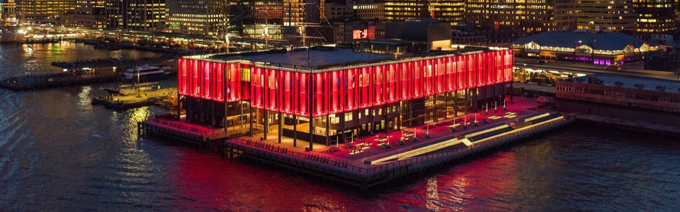 Pier 17 building at night with its red-lit facade on the East River