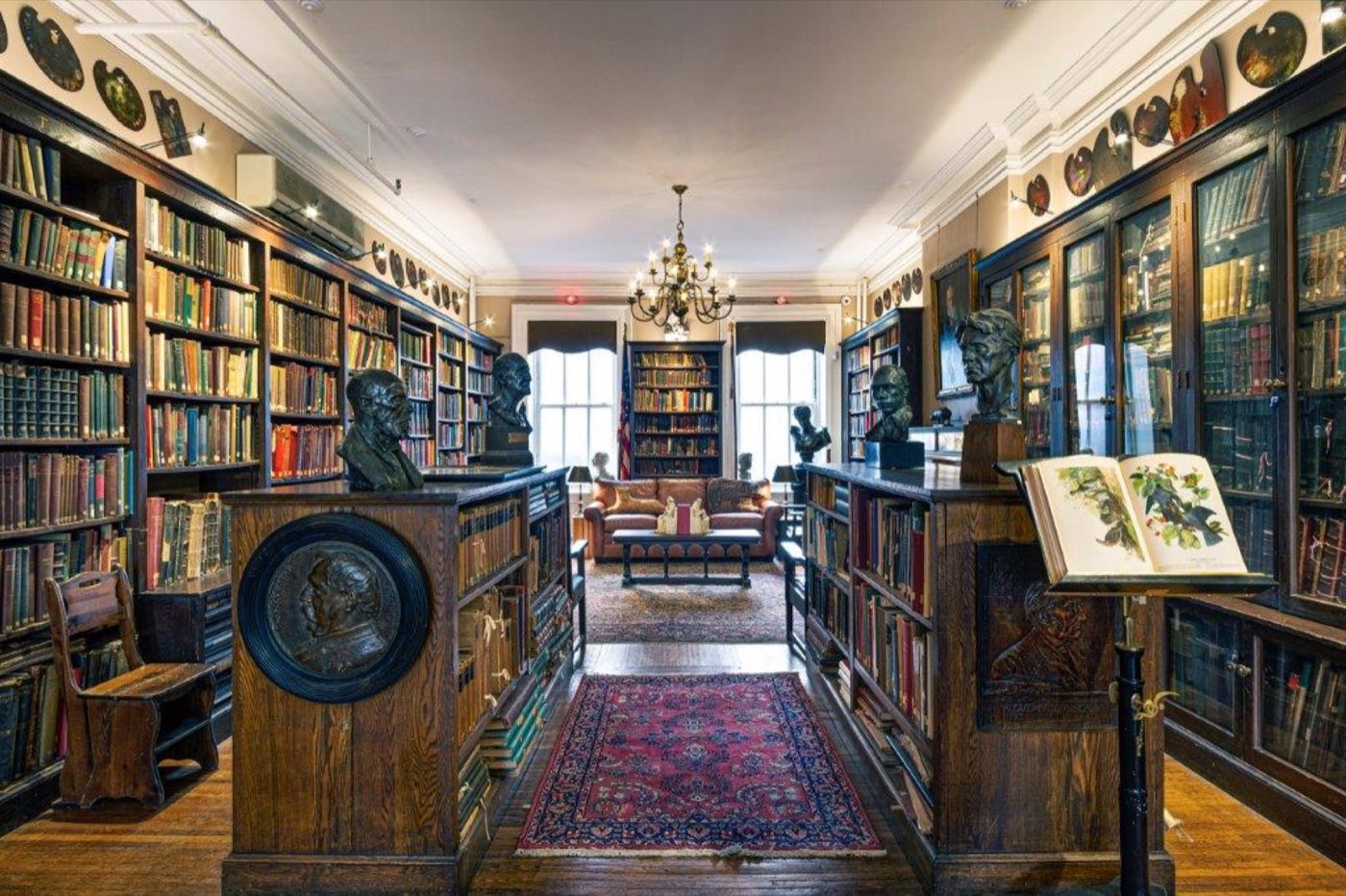 Library lined with glass-front bookcases, busts and a chandelier