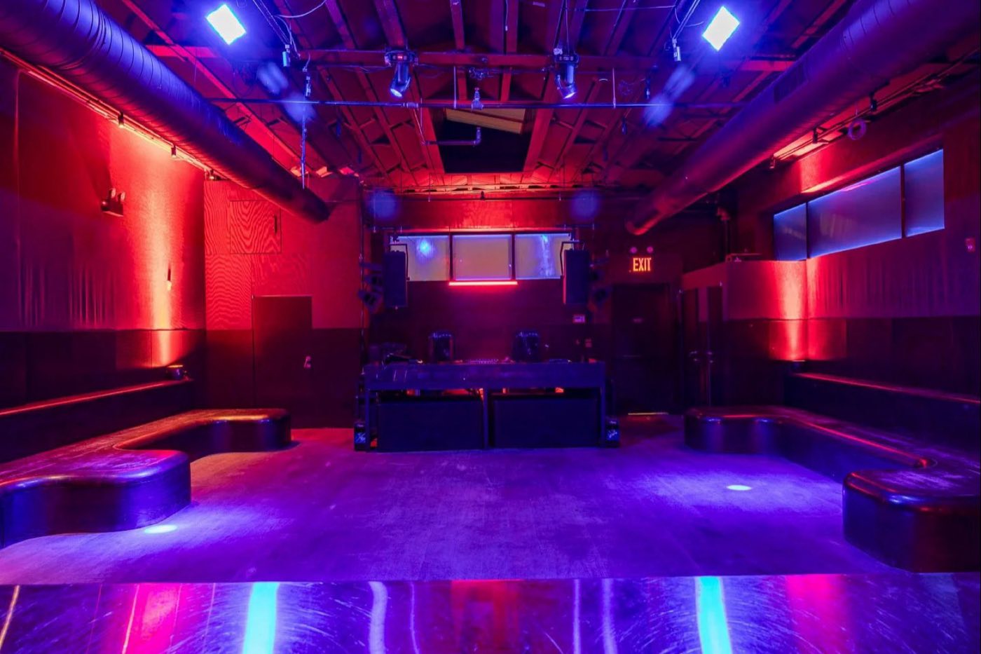 Empty main room with purple and red lighting, perimeter bench seating and DJ booth