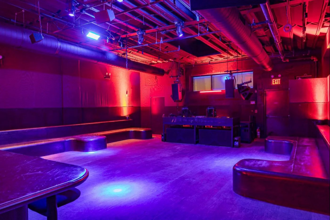 Main dance floor with curved banquettes and the DJ booth under blue light