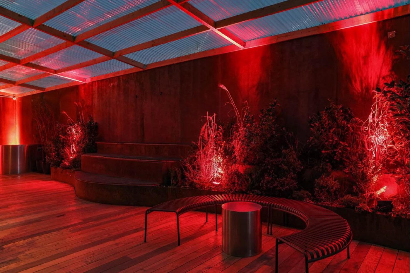Covered garden terrace with planters, curved benches and red uplighting