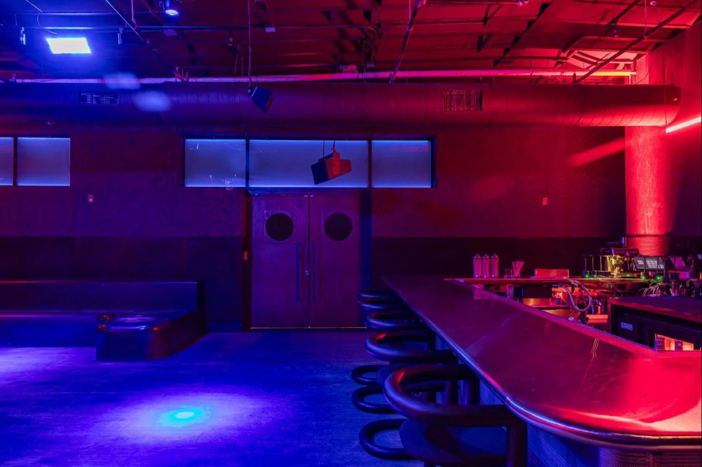 Main room seen past the bar, with the DJ booth centered under the lighting rig