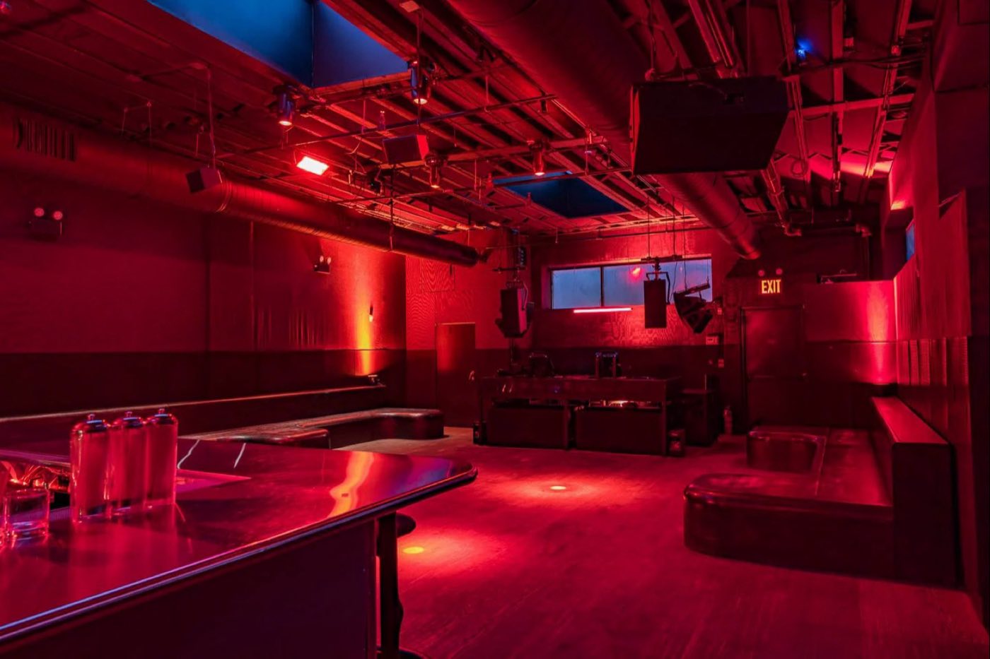 Room lit red with DJ booth, perimeter seating and suspended speaker arrays