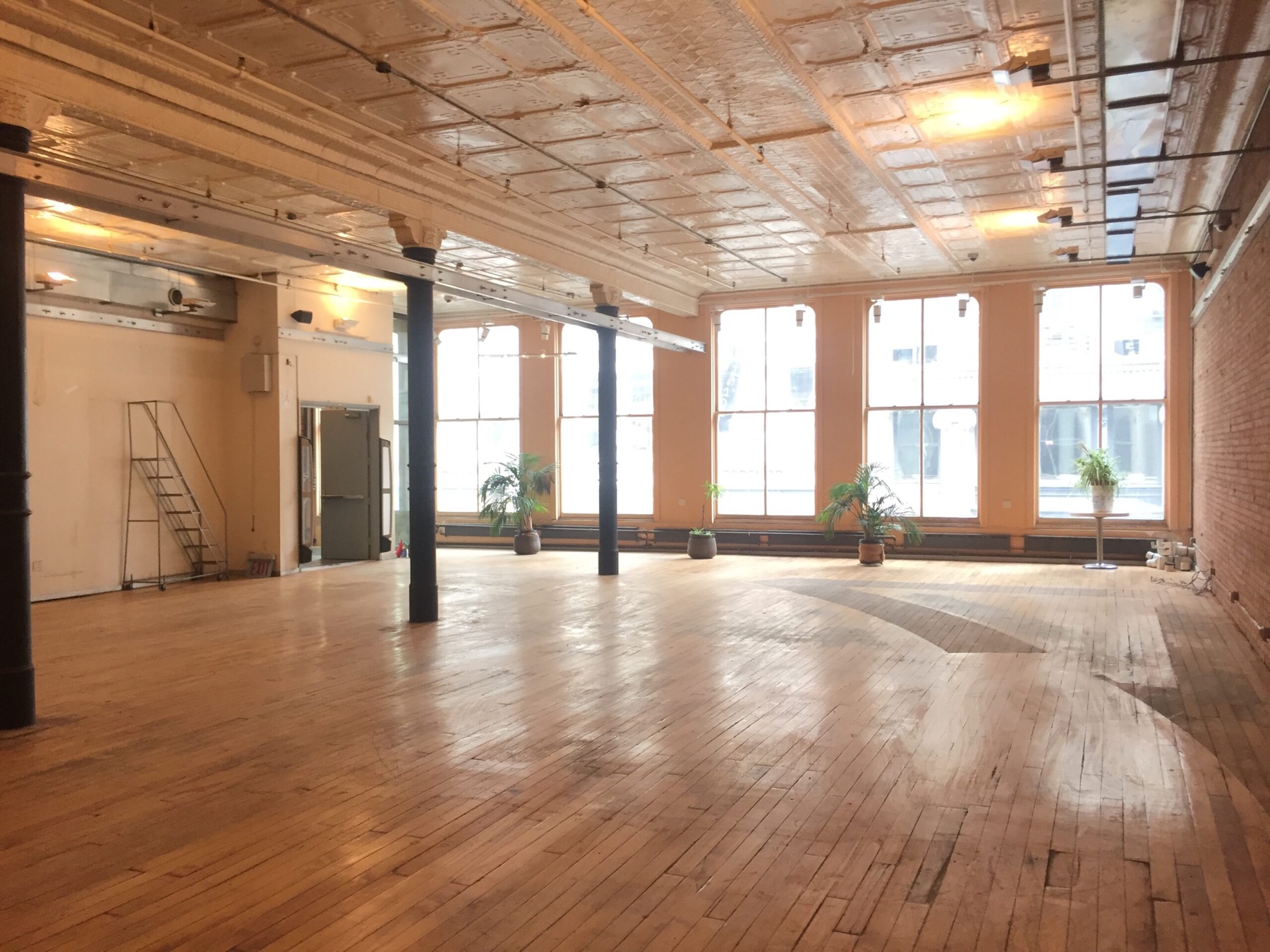 Open loft floor facing a row of arched windows under an ornate tin ceiling