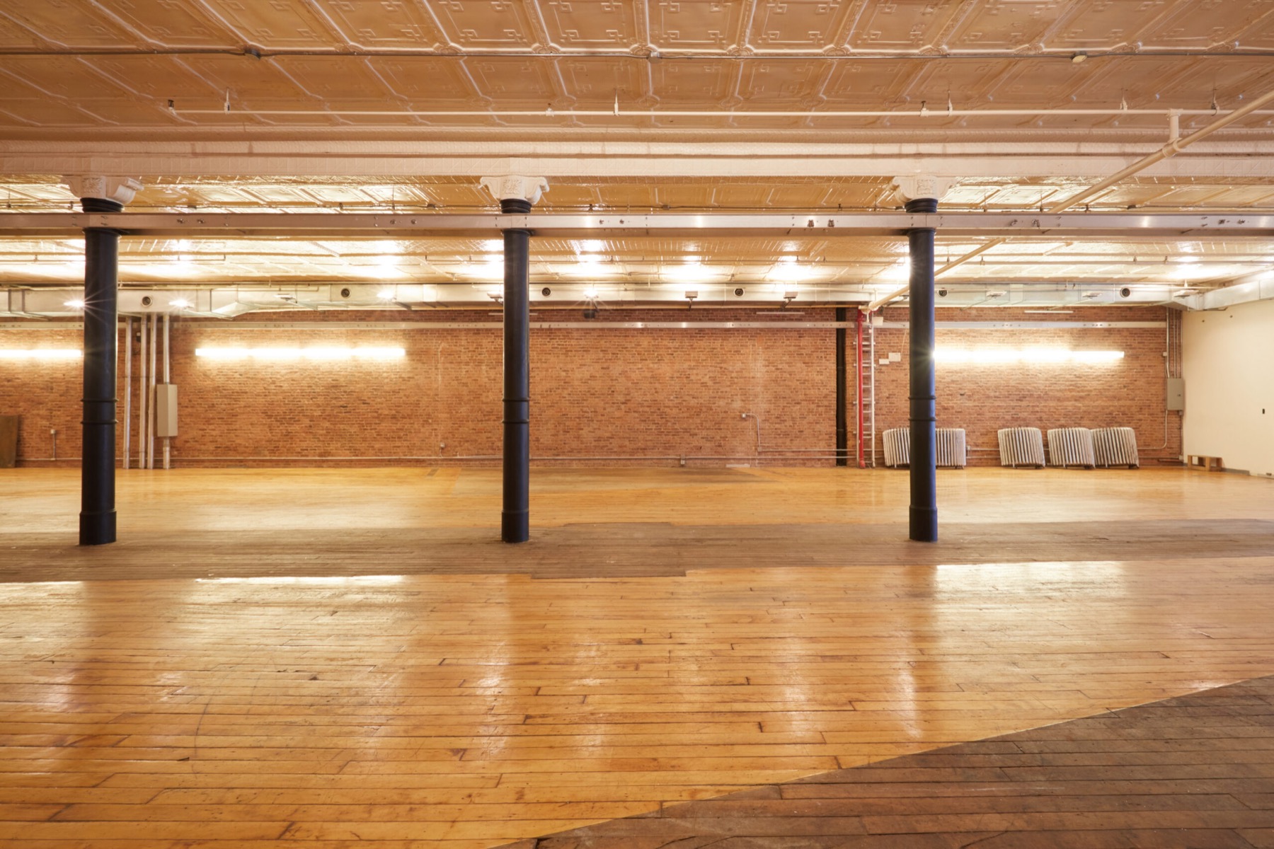 Wide empty loft room with brick back wall, iron columns and bright wood floor