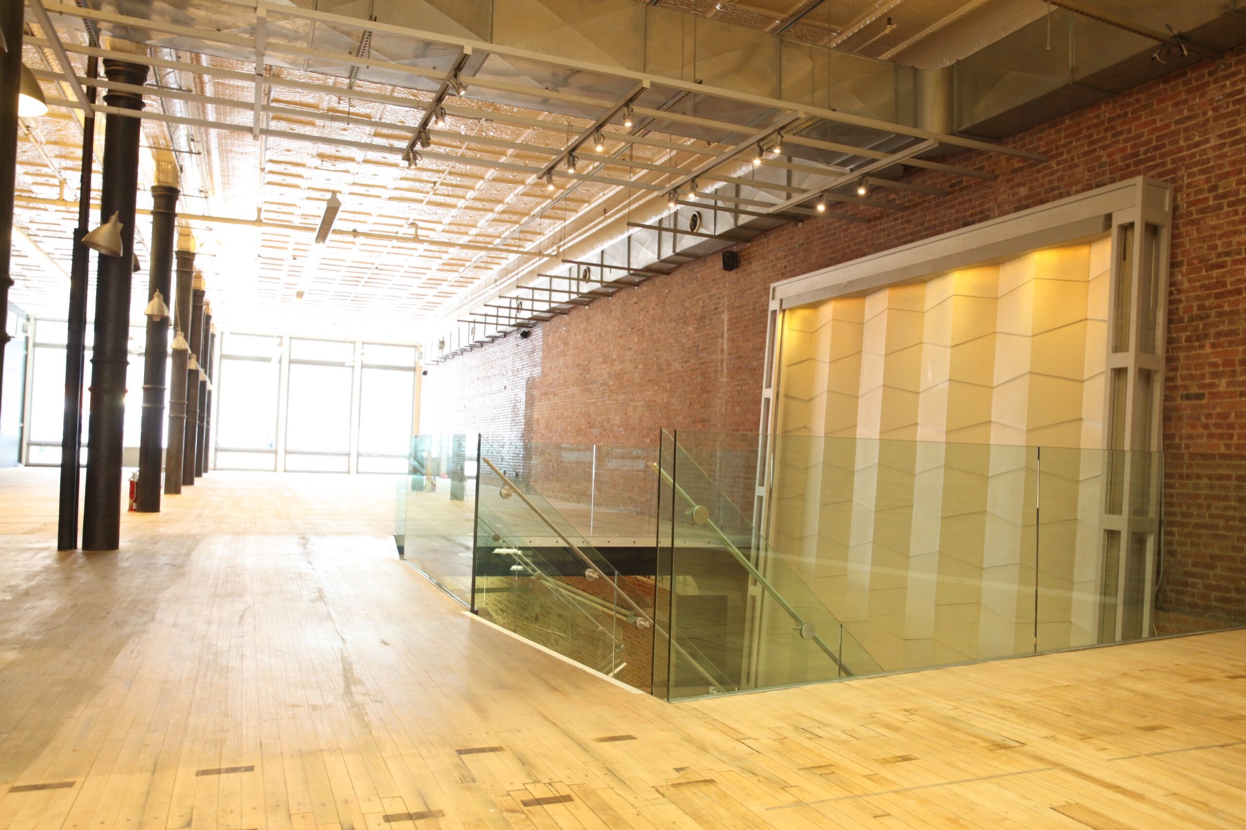 Glass-railed stair to the lower level beside a lit water wall and brick