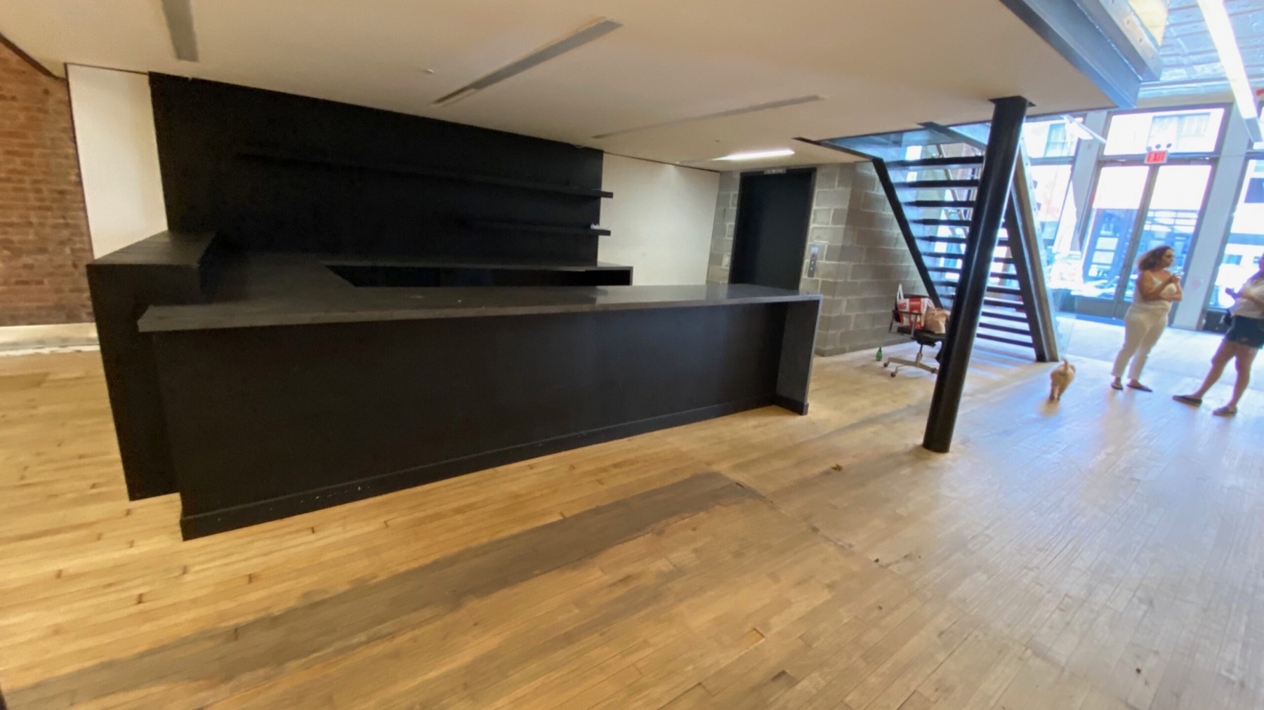 Dark built-in bar counter under a mezzanine, with storefront windows beyond