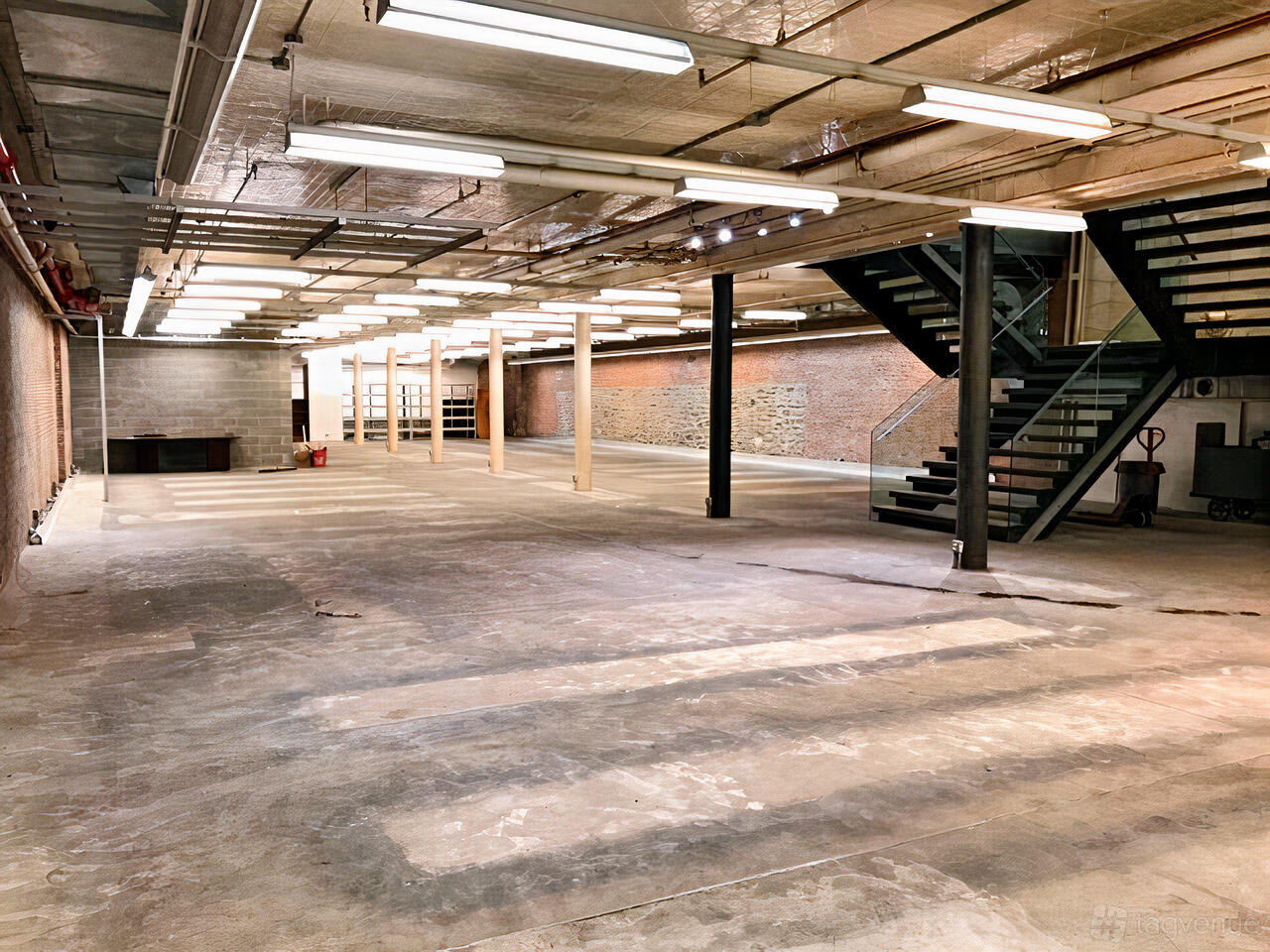 Raw lower level with concrete floor, brick walls and a stair up to the main floor