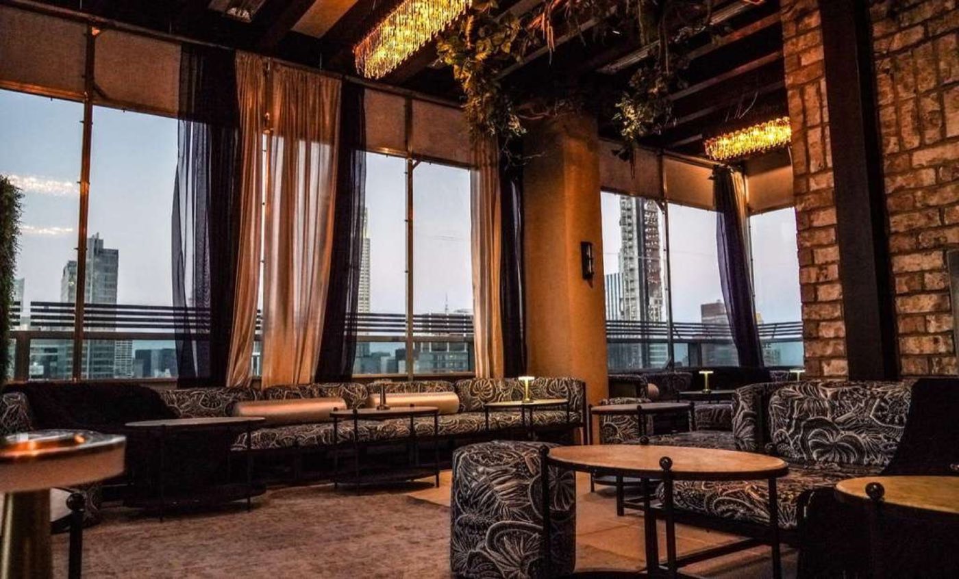 Enclosed rooftop lounge with curtains, brick columns and skyline windows