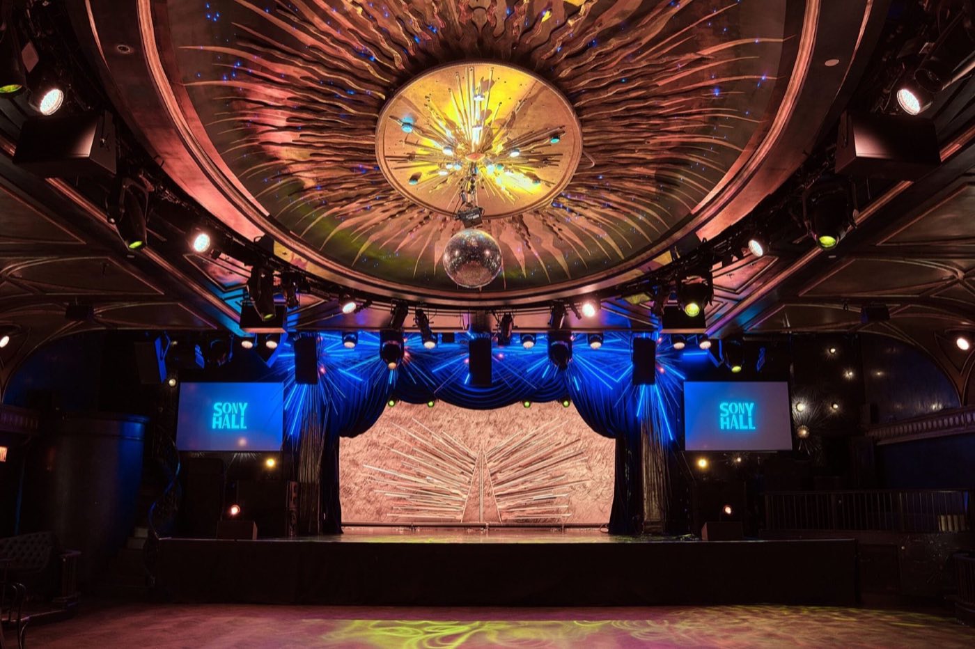 Empty main hall stage under an ornate domed ceiling with a disco ball and screens