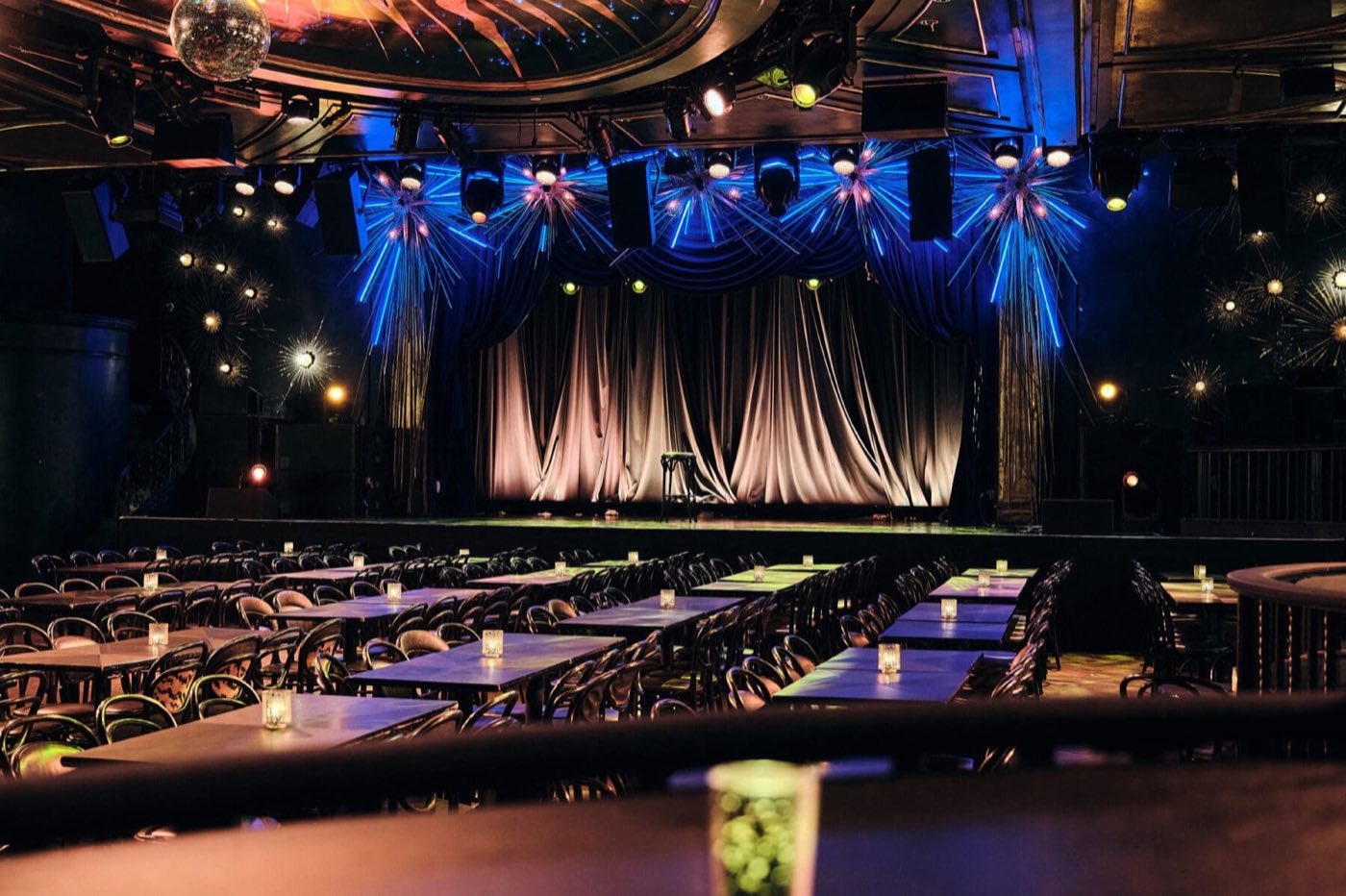 Main hall set with long banquet tables facing the curtained stage under blue lighting