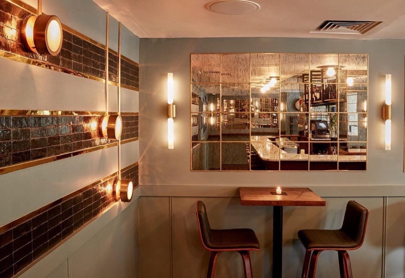 Whiskey bar corner with brass sconces, tiled wall stripes and a mirrored panel