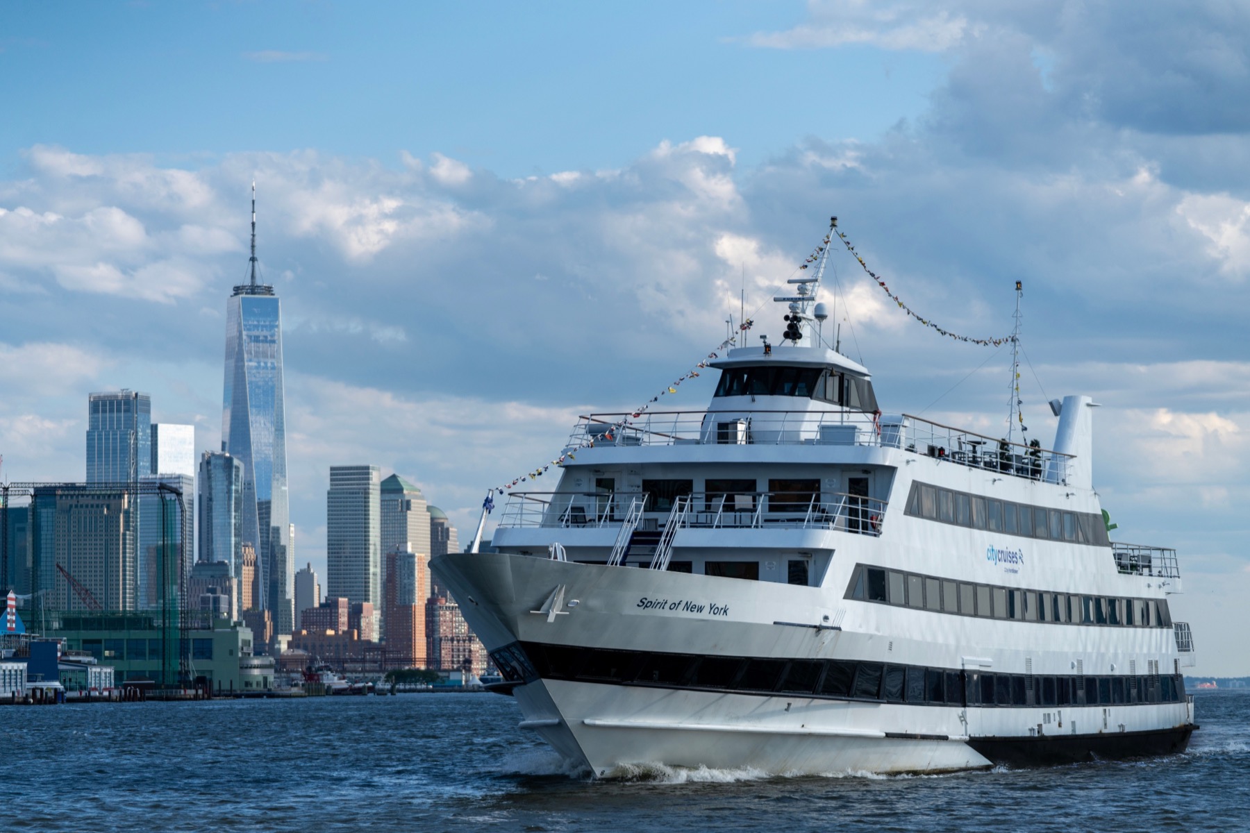 Three-deck white yacht cruising the Hudson with the Lower Manhattan skyline behind it