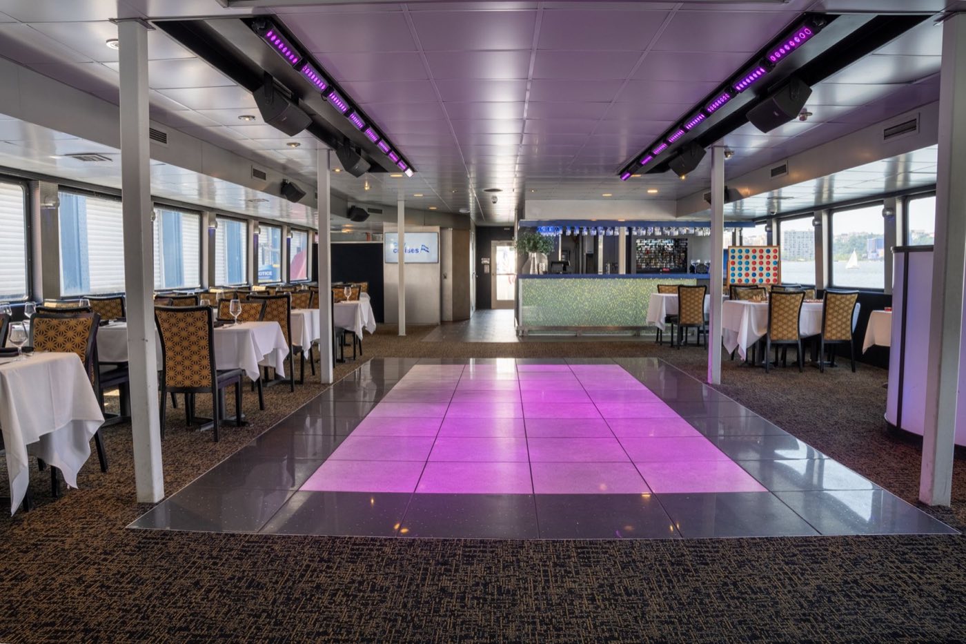 Lit dance floor surrounded by dining tables with a bar and river windows