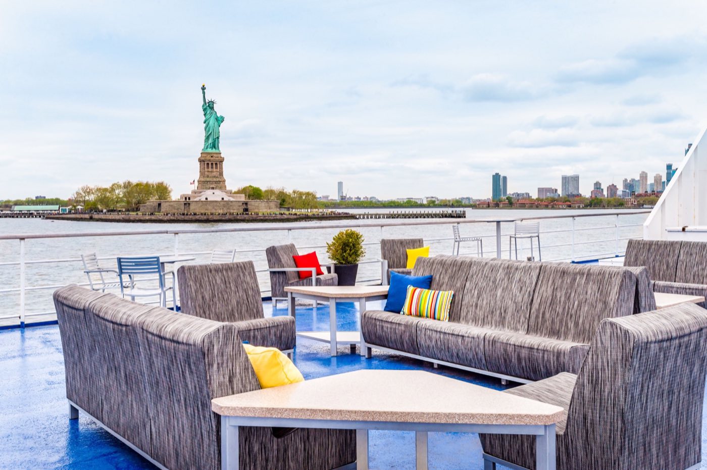 Open-air top deck lounge seating facing the Statue of Liberty across the harbor