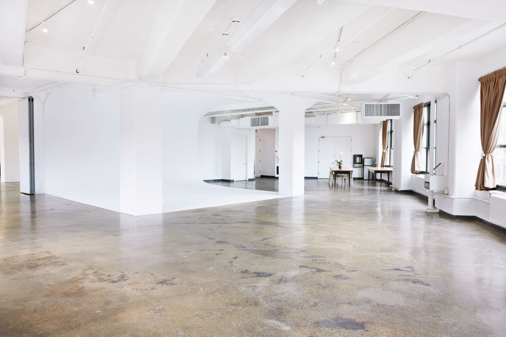 Empty daylit studio with concrete floor, white cyclorama and tall windows