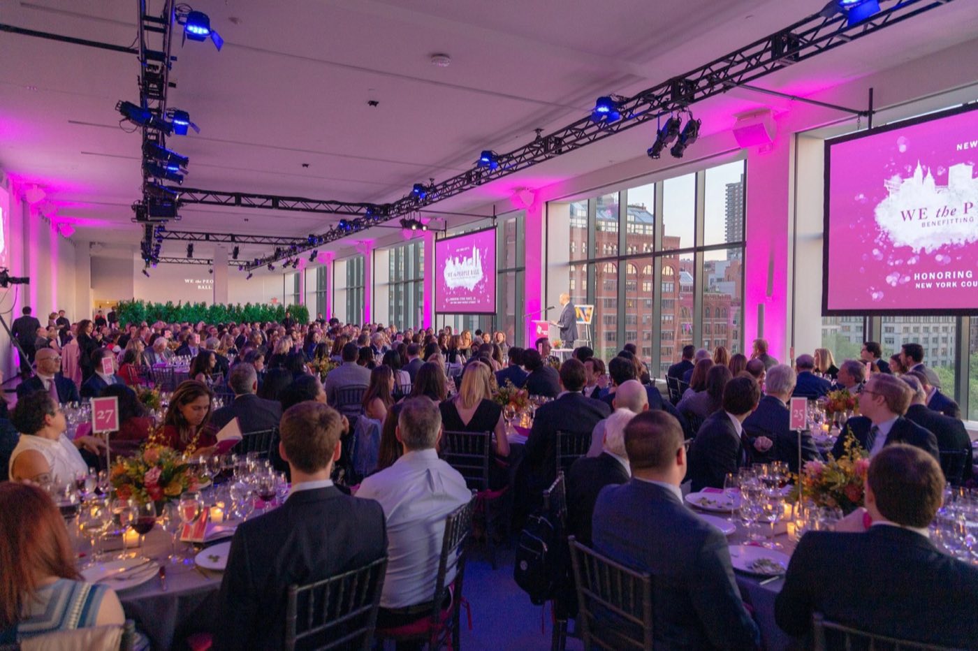Gala dinner in the Studios with round tables, stage screens and pink uplighting
