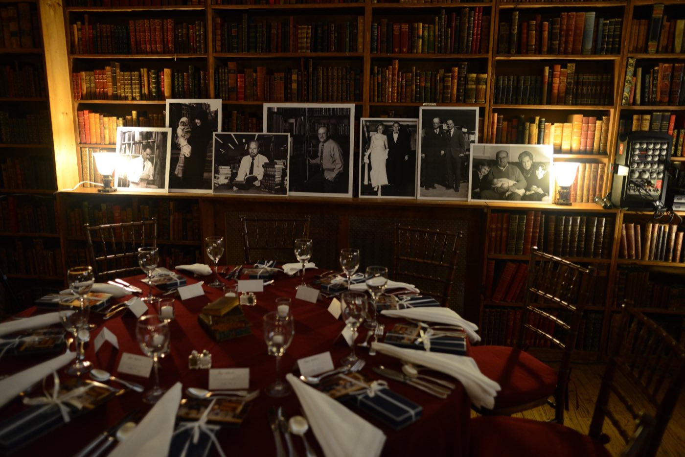 Round dinner table with red linens before shelves of leather-bound books and framed photos