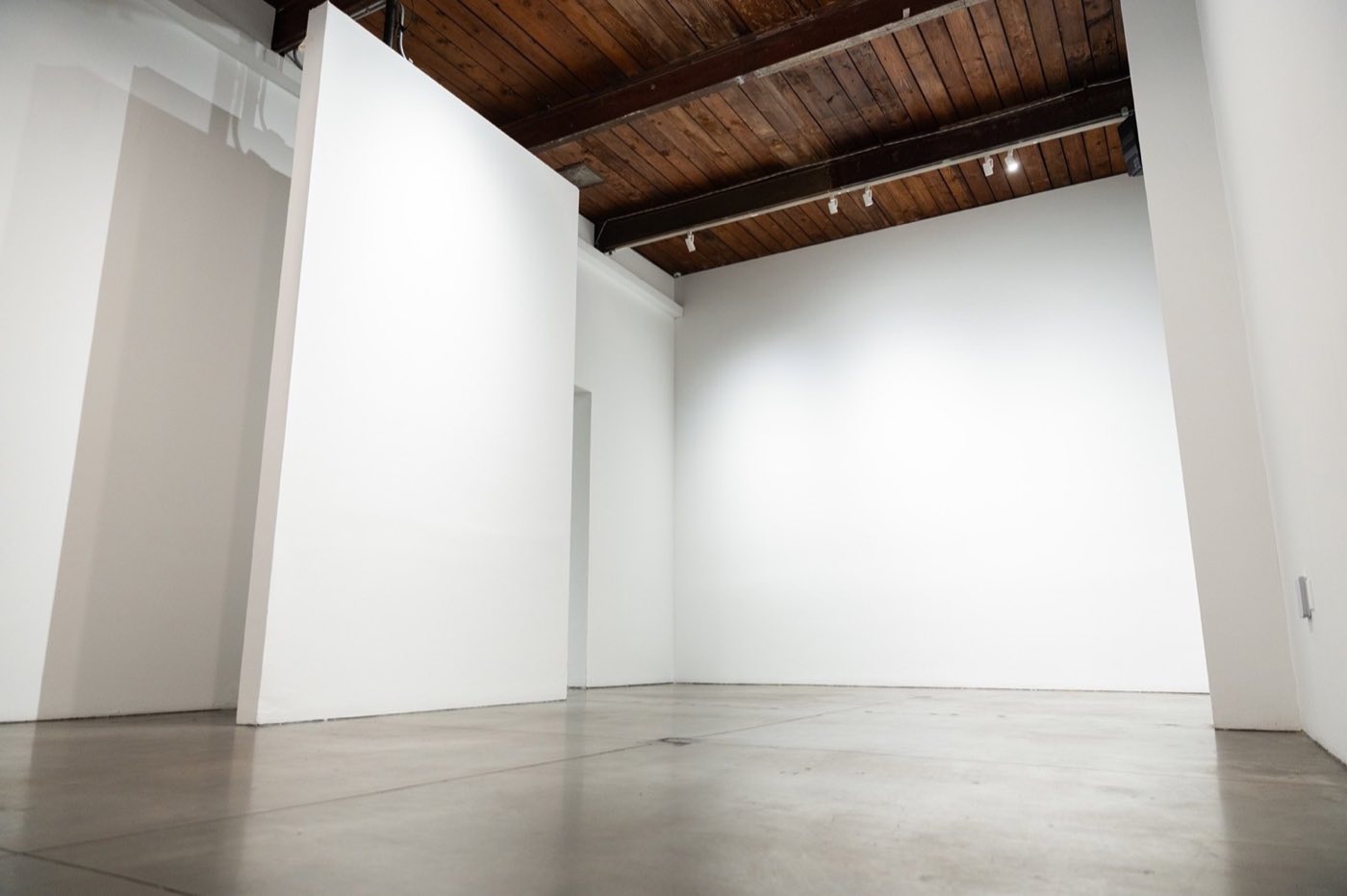 Secondary white-walled studio room with wood-beamed ceiling and polished concrete floor