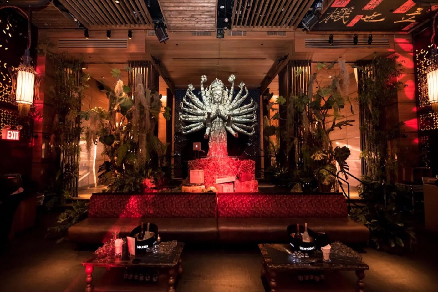 Lounge seating area in front of a red-lit multi-armed statue surrounded by plants