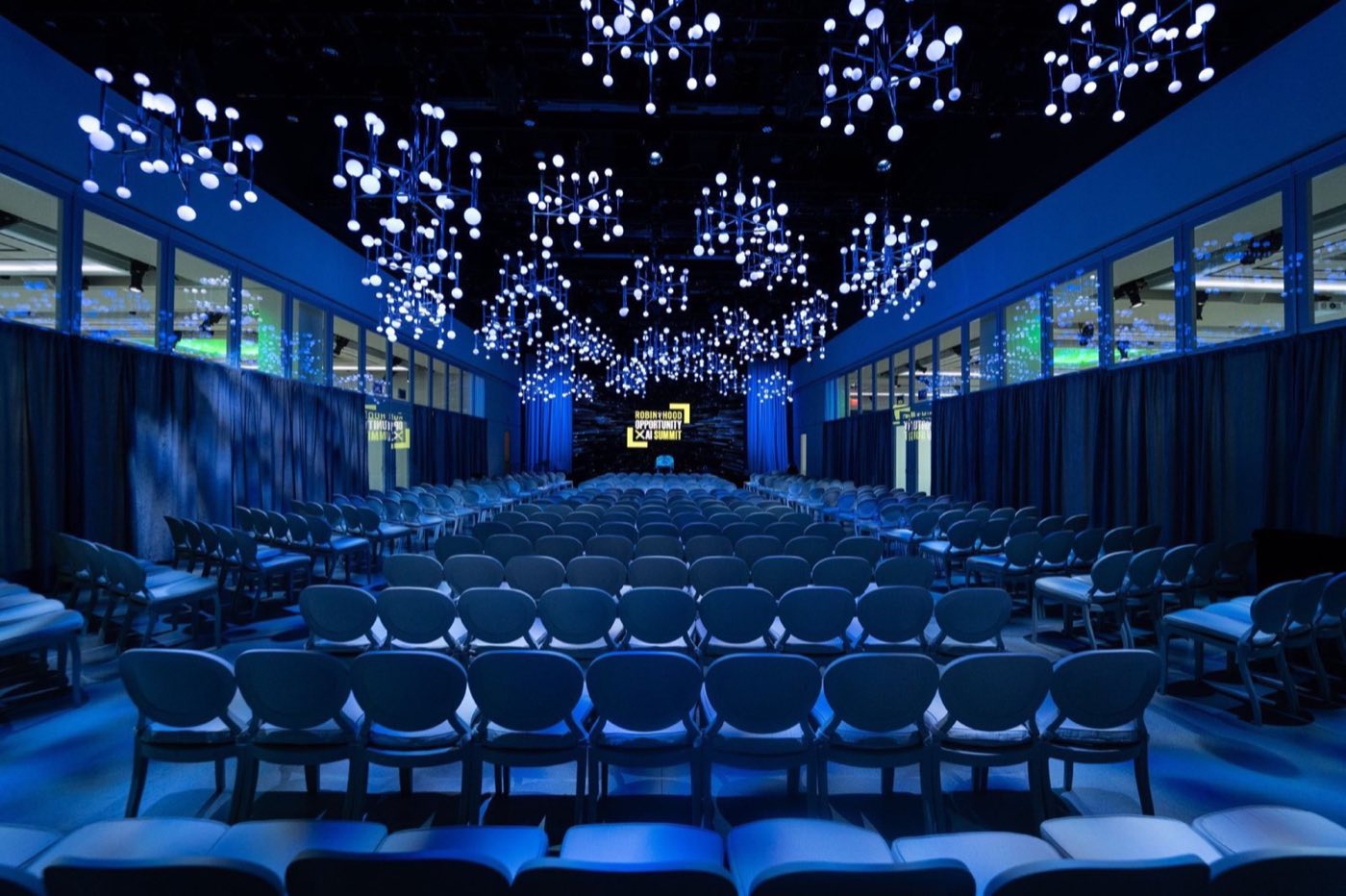 Long glass-walled hall in theater seating under a ceiling of suspended light orbs