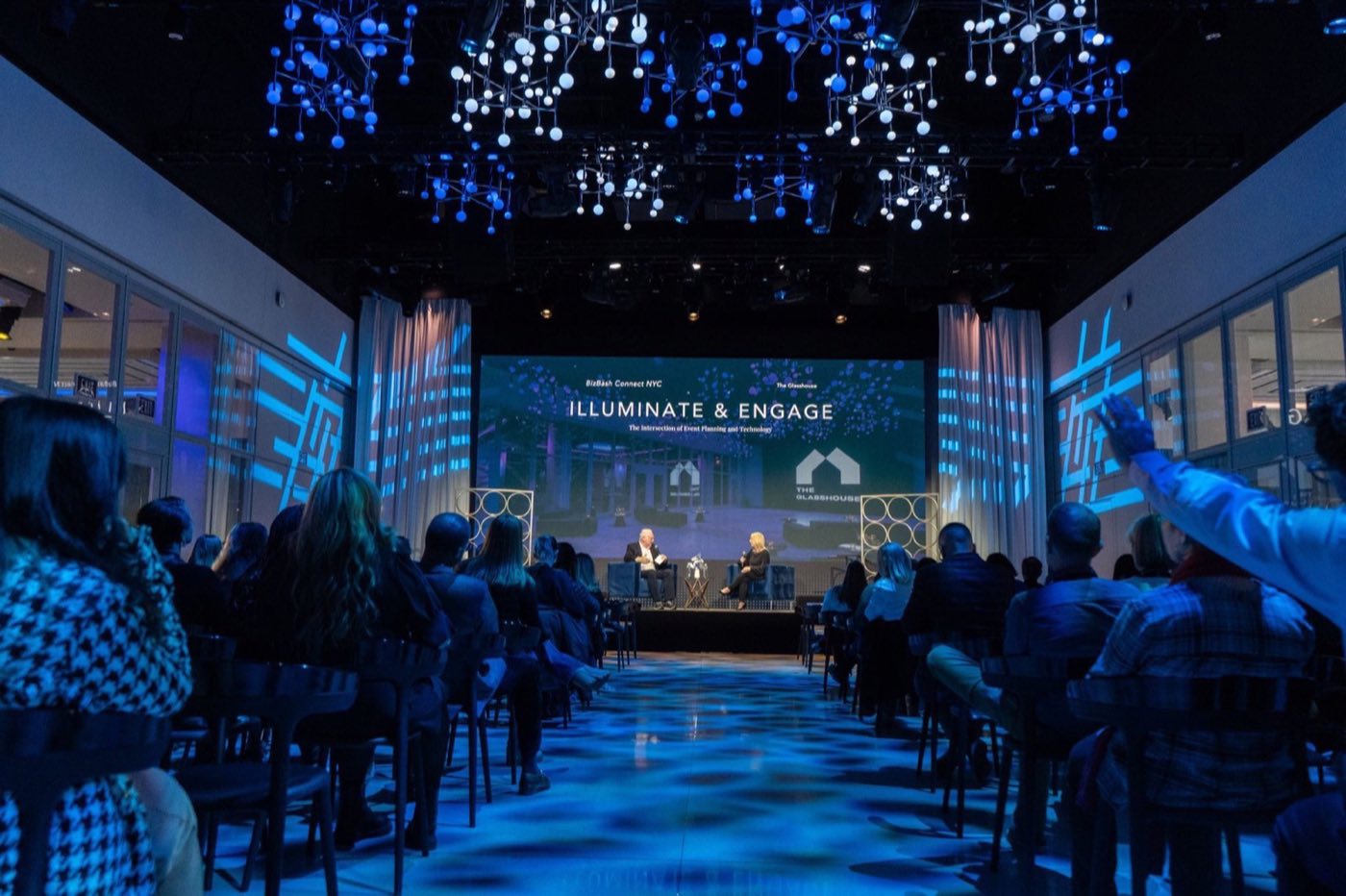 Conference session with a center aisle, stage screen and blue ceiling lights