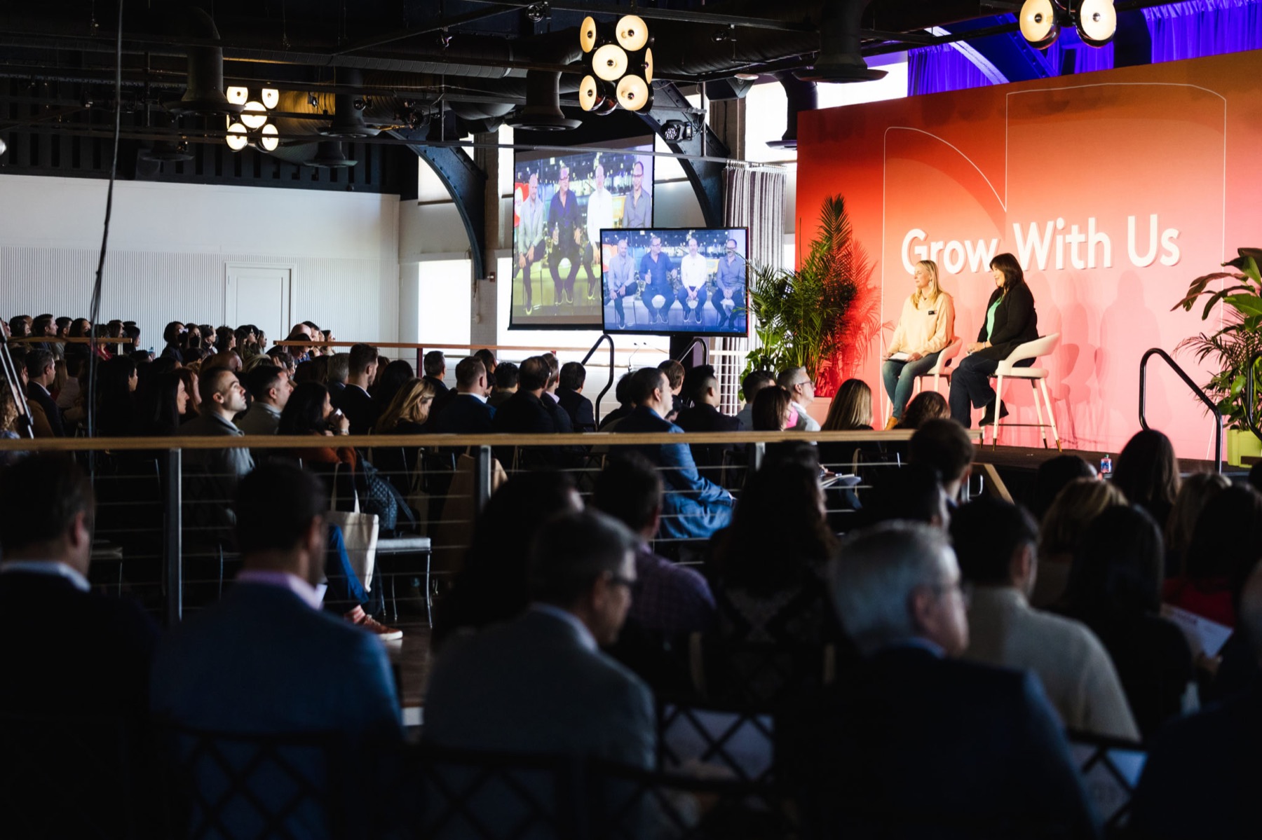 Panel discussion on a stage with screens and a seated audience in the main room