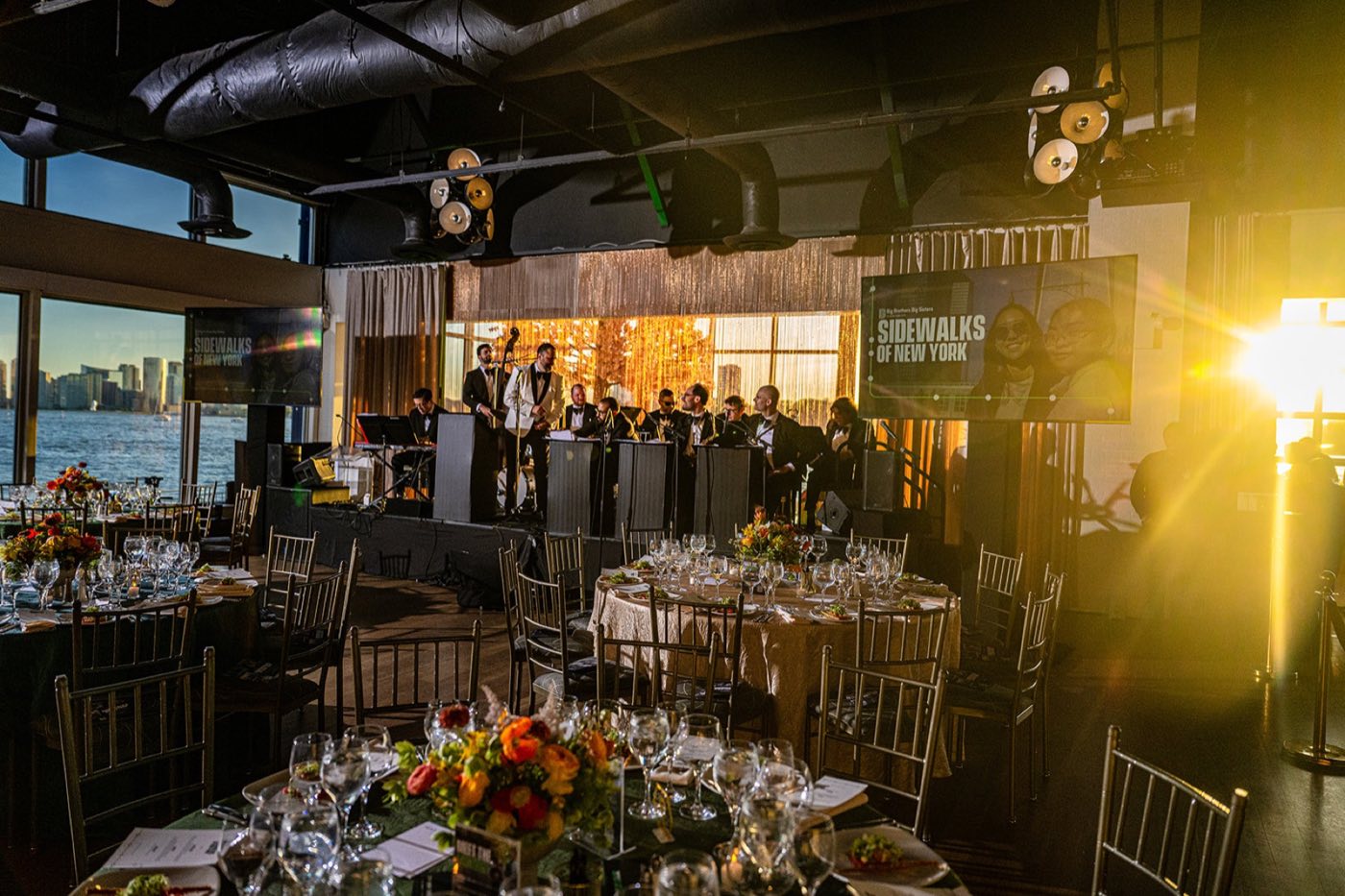Main room set with round dinner tables and a band on stage at sunset