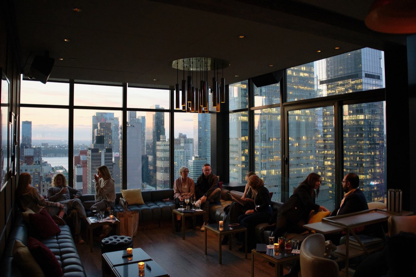 Guests gathered on banquettes in the Main Lounge at dusk with city lights