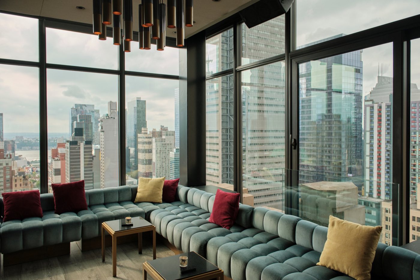 Corner of the lounge with green banquettes, throw pillows and wide Midtown views