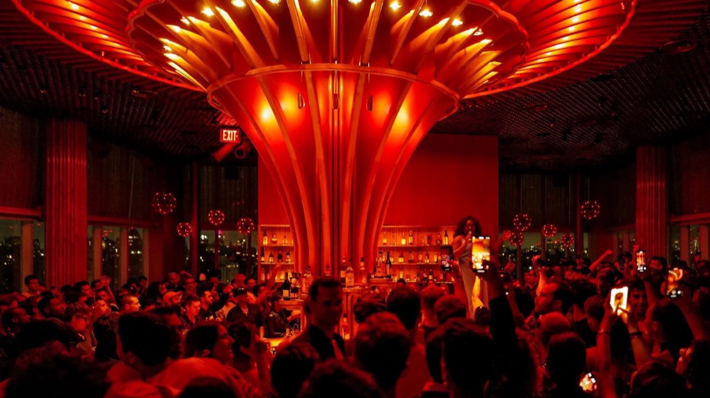 Top-floor ballroom lit red during a packed party beneath a sculptural gold ceiling