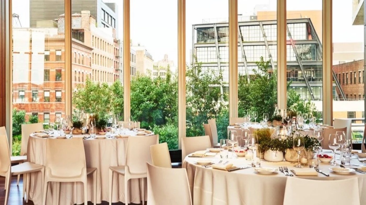 Glass-walled room set with round dinner tables beside the High Line greenery