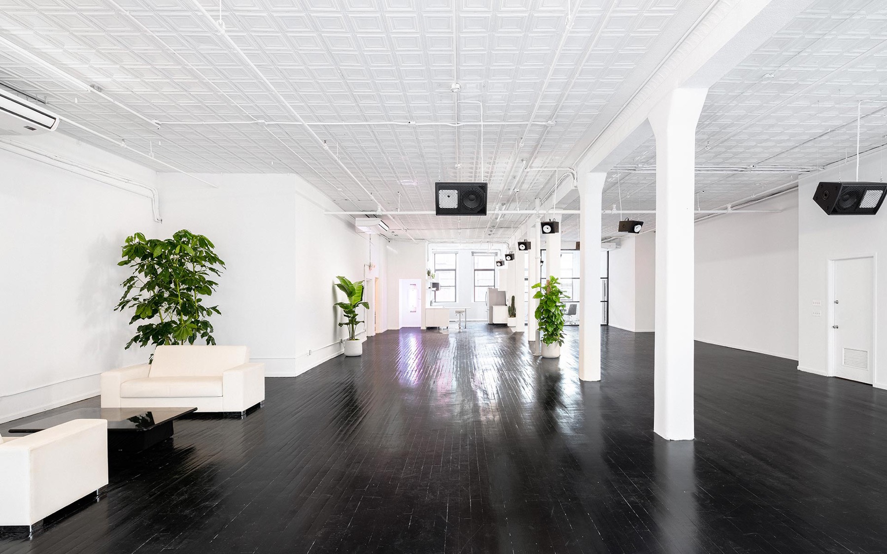 Bright white loft with black wood floors, cast iron columns, lounge seating and plants