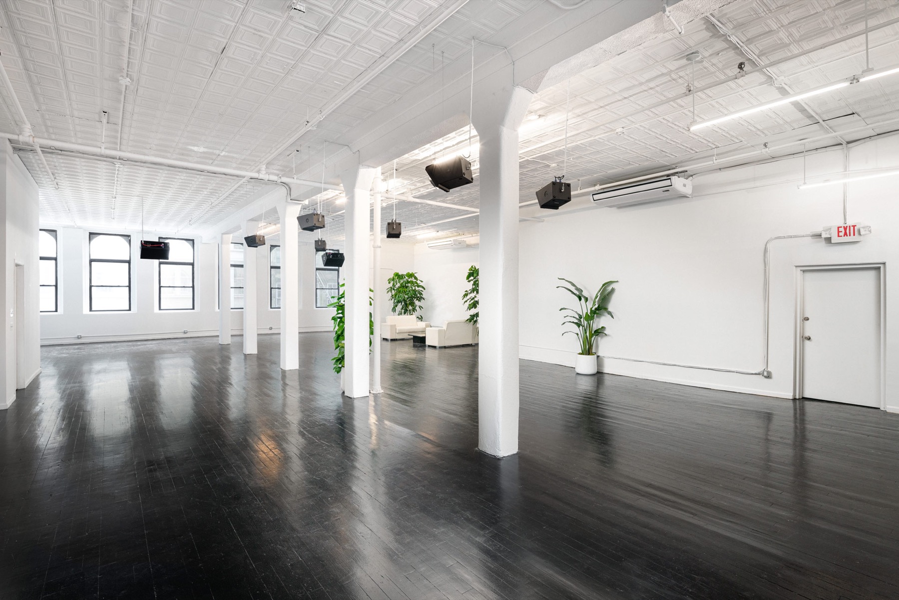 Open industrial loft with white columns, tin ceiling, glossy black floor and arched windows