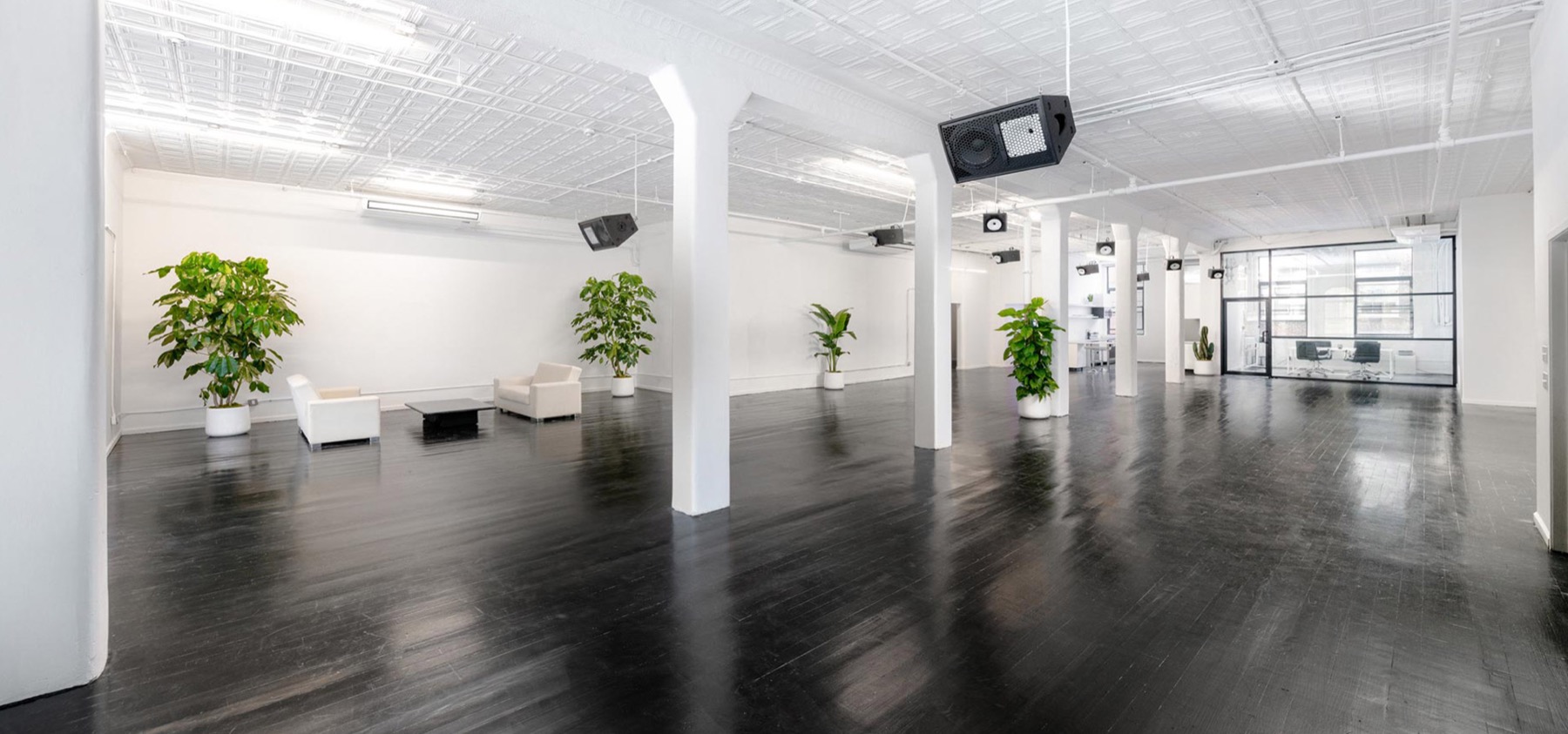 Wide view of an empty white loft studio with dark floors and a glass meeting room