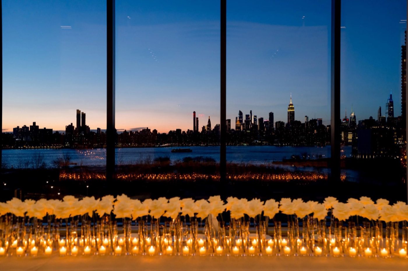 Candlelit reception with rows of flowers along the windows and the skyline at dusk
