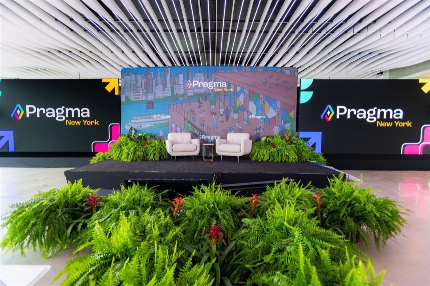 Stage set for a conference talk with branded screens, armchairs and fern planters