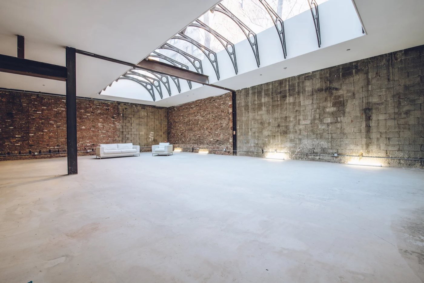 Empty open floor with exposed brick walls under a long arched glass skylight
