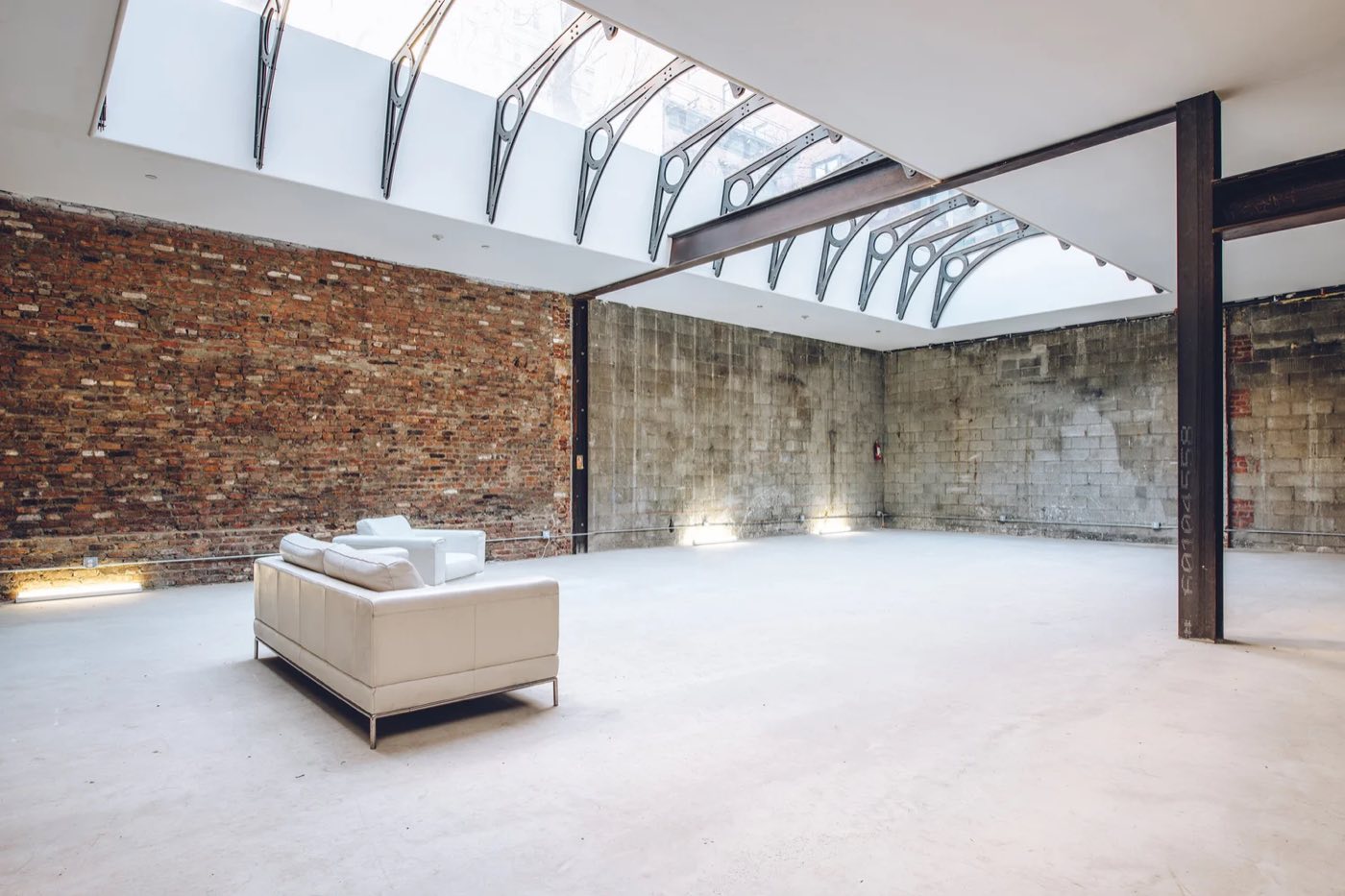 Skylit room with brick and concrete walls, steel columns and a white sofa