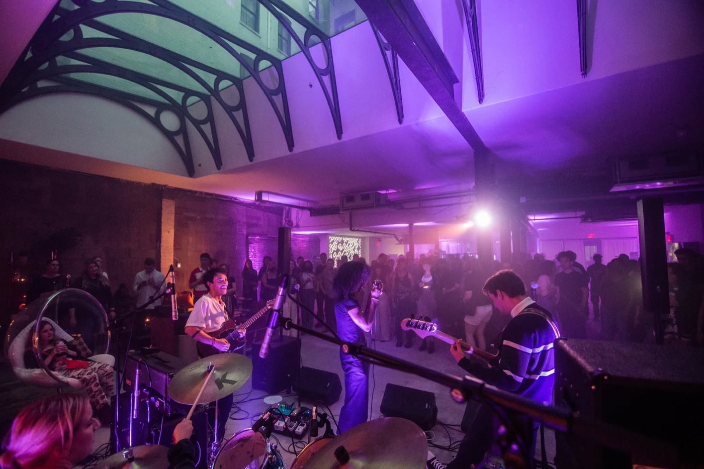 Live band playing to a standing crowd in purple light under the arched skylight