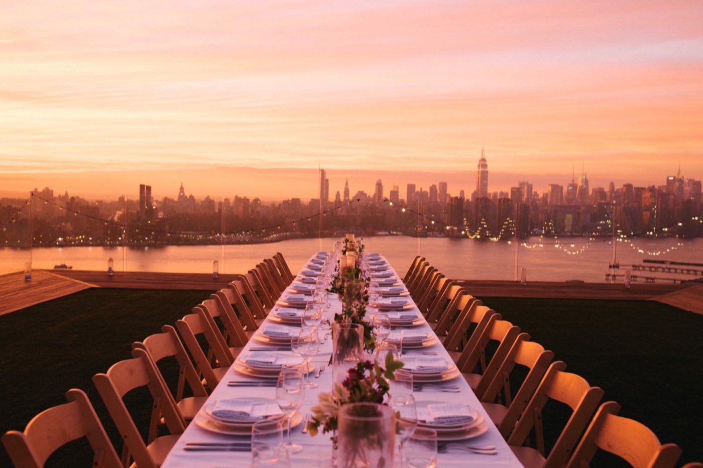 Long banquet table set on the rooftop at sunset with the Manhattan skyline behind