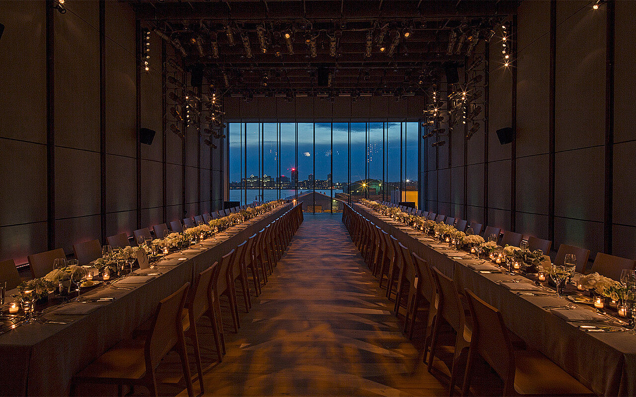 Long banquet tables in the dark theater facing a window over the Hudson at dusk