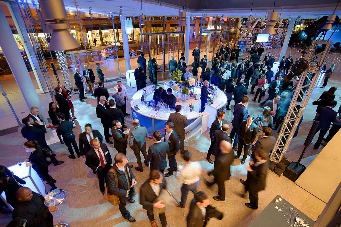Reception crowd around a lit round bar seen from above in the lobby